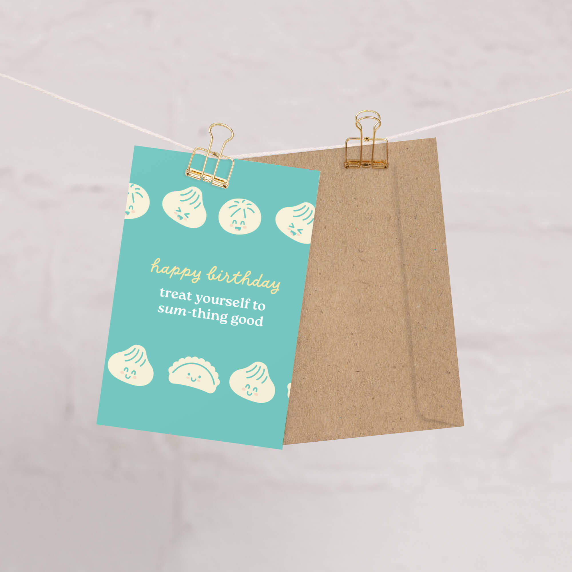 Greeting card with 'happy birthday' message on a teal background, hanging on a string with a paper clip.