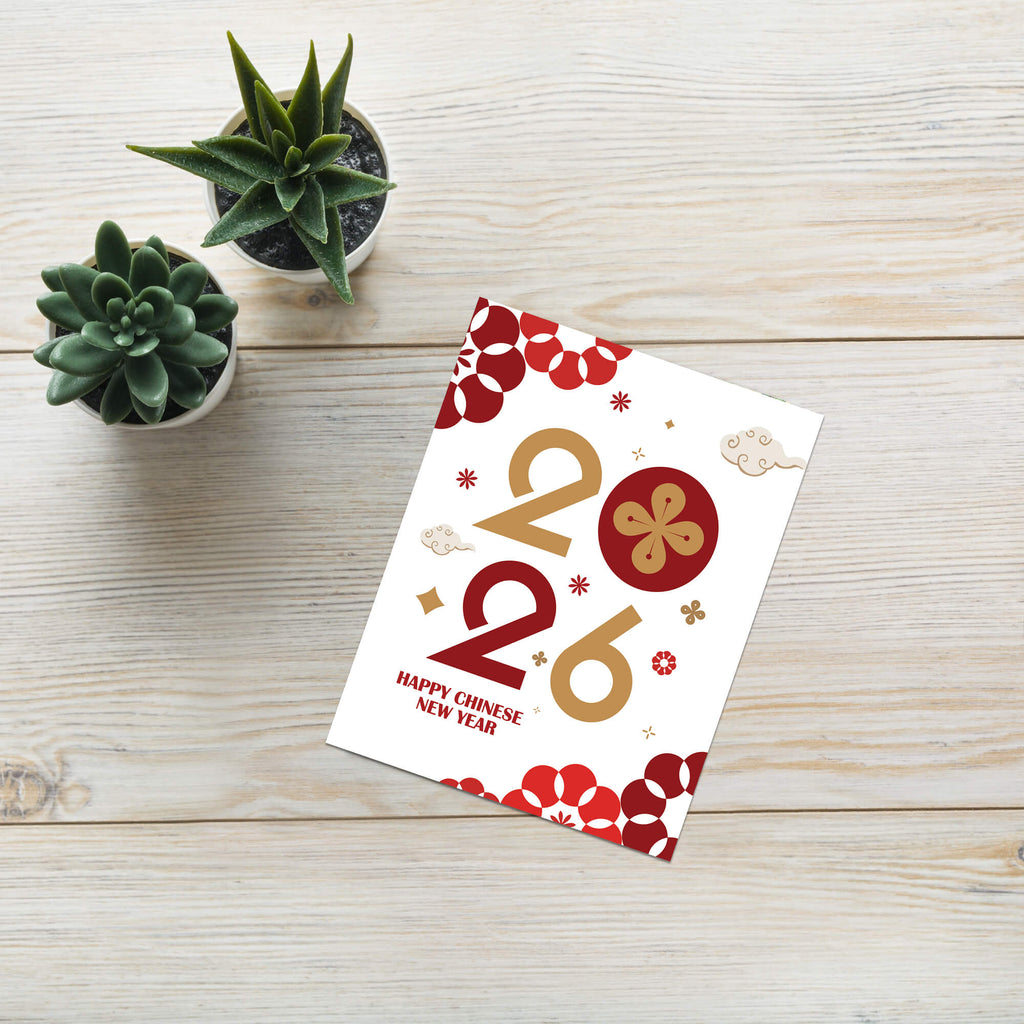 Card with 'Happy Chinese New Year' text and floral designs on a wooden surface with small potted plants.