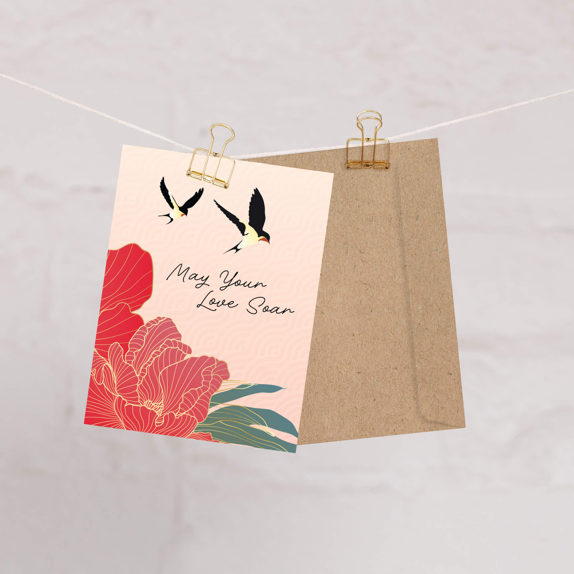 Floral and bird design on a pink card with a brown envelope, clipped to a string.