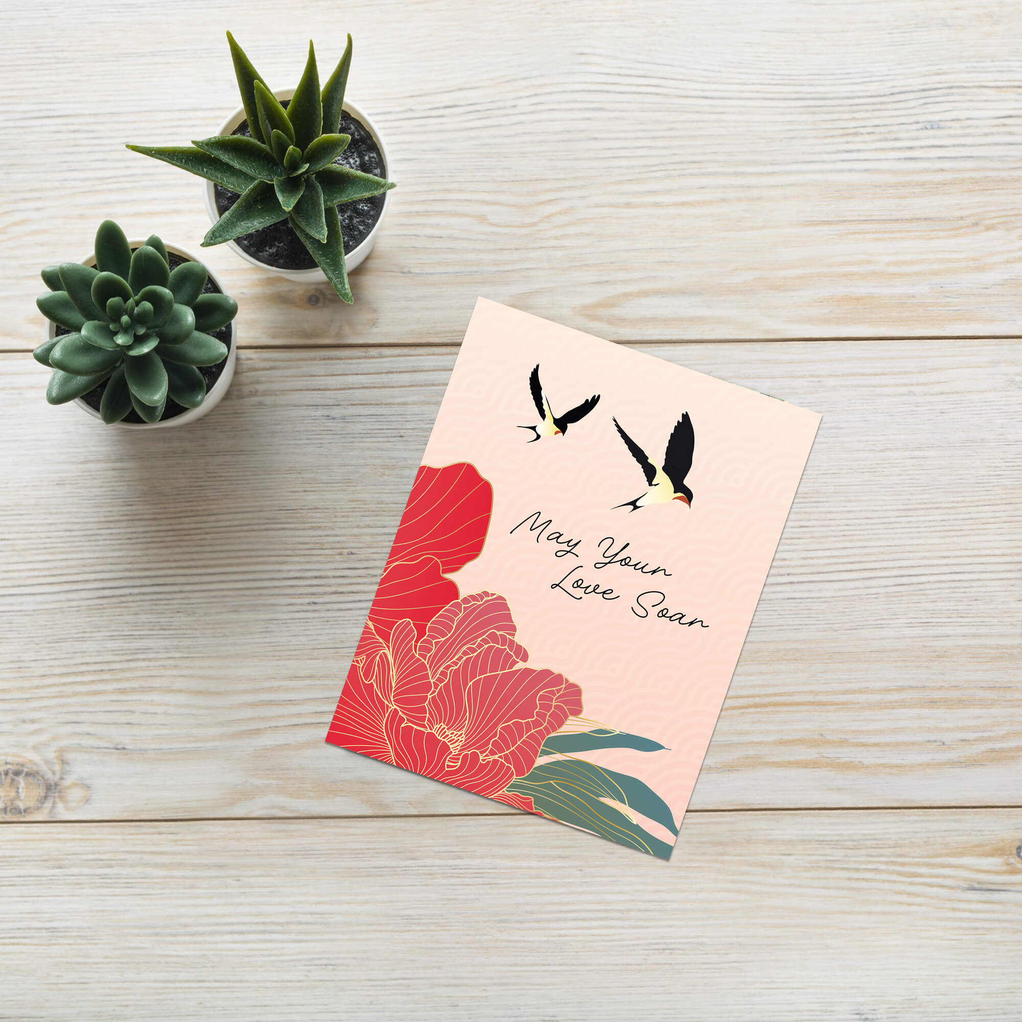Greeting card with floral design and text on a wooden surface with small plants.