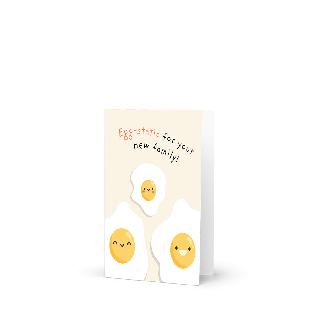 A funny baby shower card featuring three cute cartoon fried eggs with smiling faces on a cream background, with the text 'Egg-static for your new family!' in orange and black script.