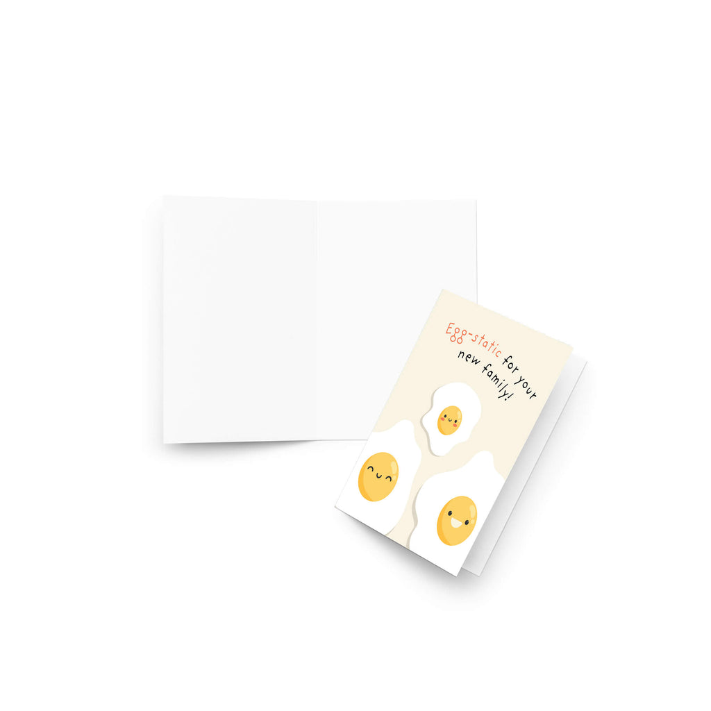 A funny baby shower card with a white envelope on a clean white background. The card features three cute cartoon fried eggs with smiling faces on a cream-colored background, with the text 'Eggs!sthetic new family!'.