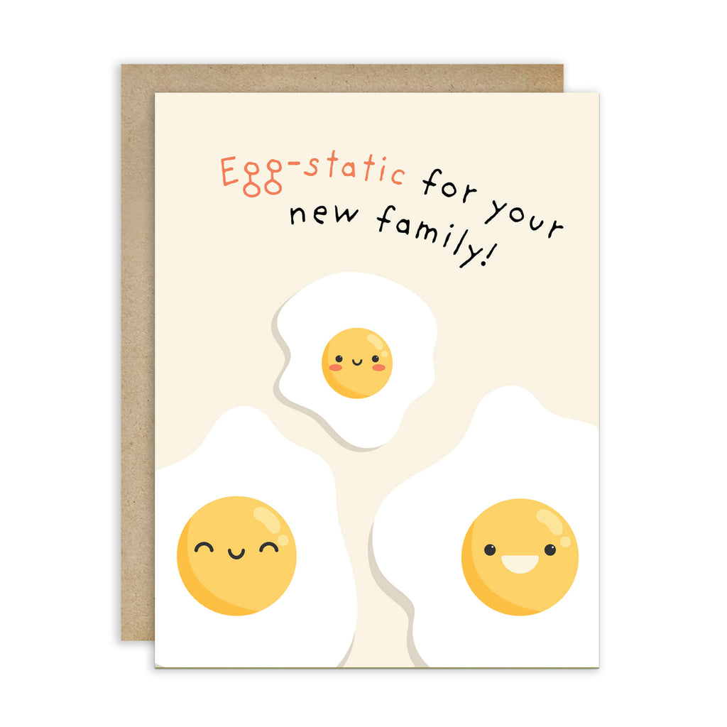 A funny baby shower card with a kraft envelope, featuring the text 'Egg-static for your new family!' above three cute cartoon fried eggs on a cream background.