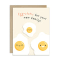 A funny baby shower card with a kraft envelope, featuring the text 'Egg-static for your new family!' above three cute cartoon fried eggs on a cream background.