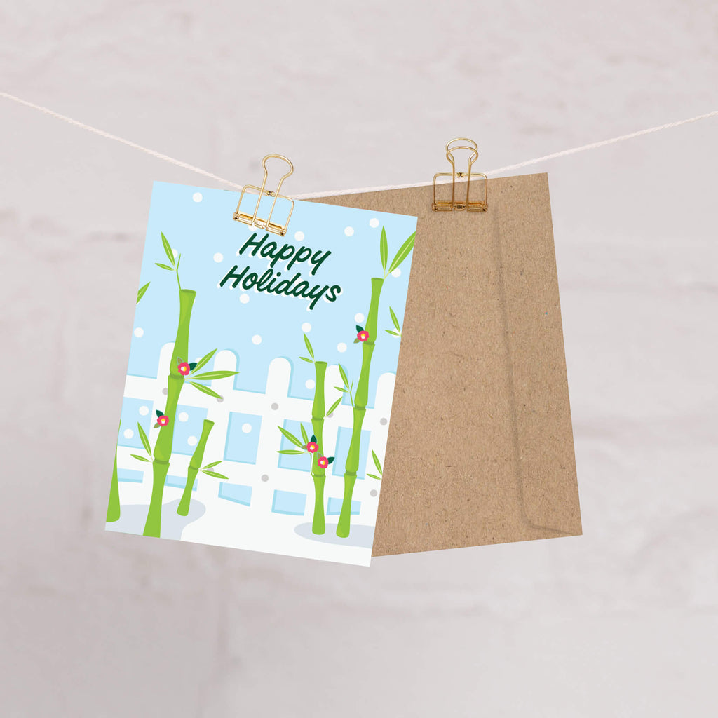 Greeting card with bamboo design and 'Happy Holidays' text, attached to a string with a brown envelope.