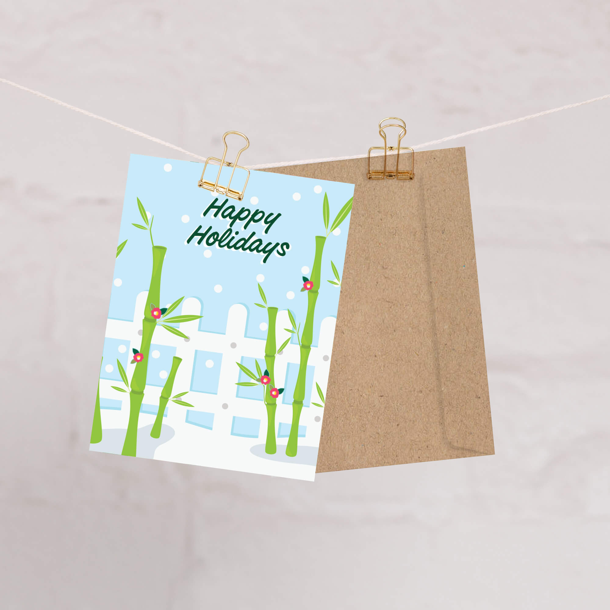 Greeting card with bamboo design and 'Happy Holidays' text, attached to a string with a brown envelope.