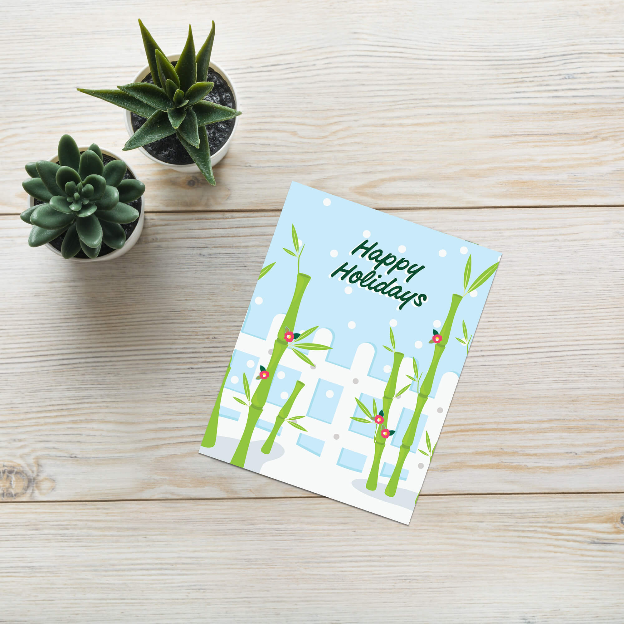 Greeting card with bamboo design and 'Happy Holidays' text on a wooden surface with potted plants.