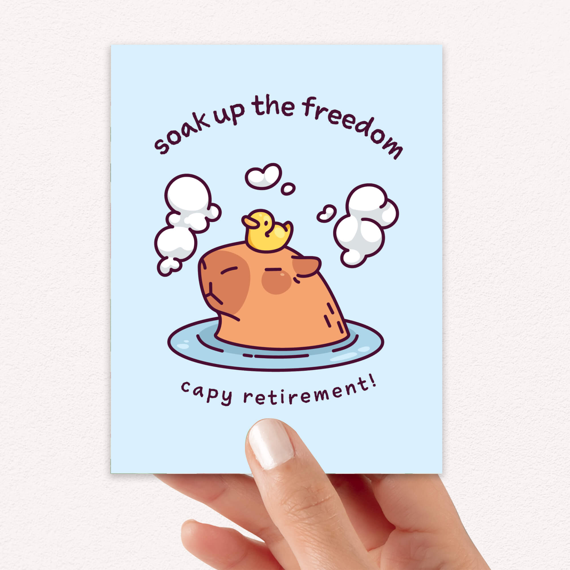 Card with a cartoon dog and duck in water, text 'soak up the freedom capy retirement!' held by a hand.