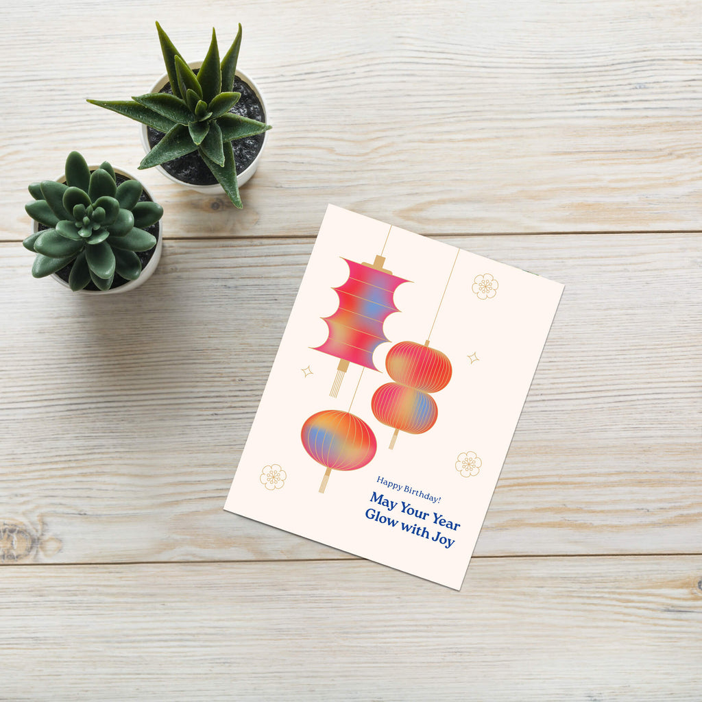 Greeting card with colorful designs on a wooden surface with small potted plants.