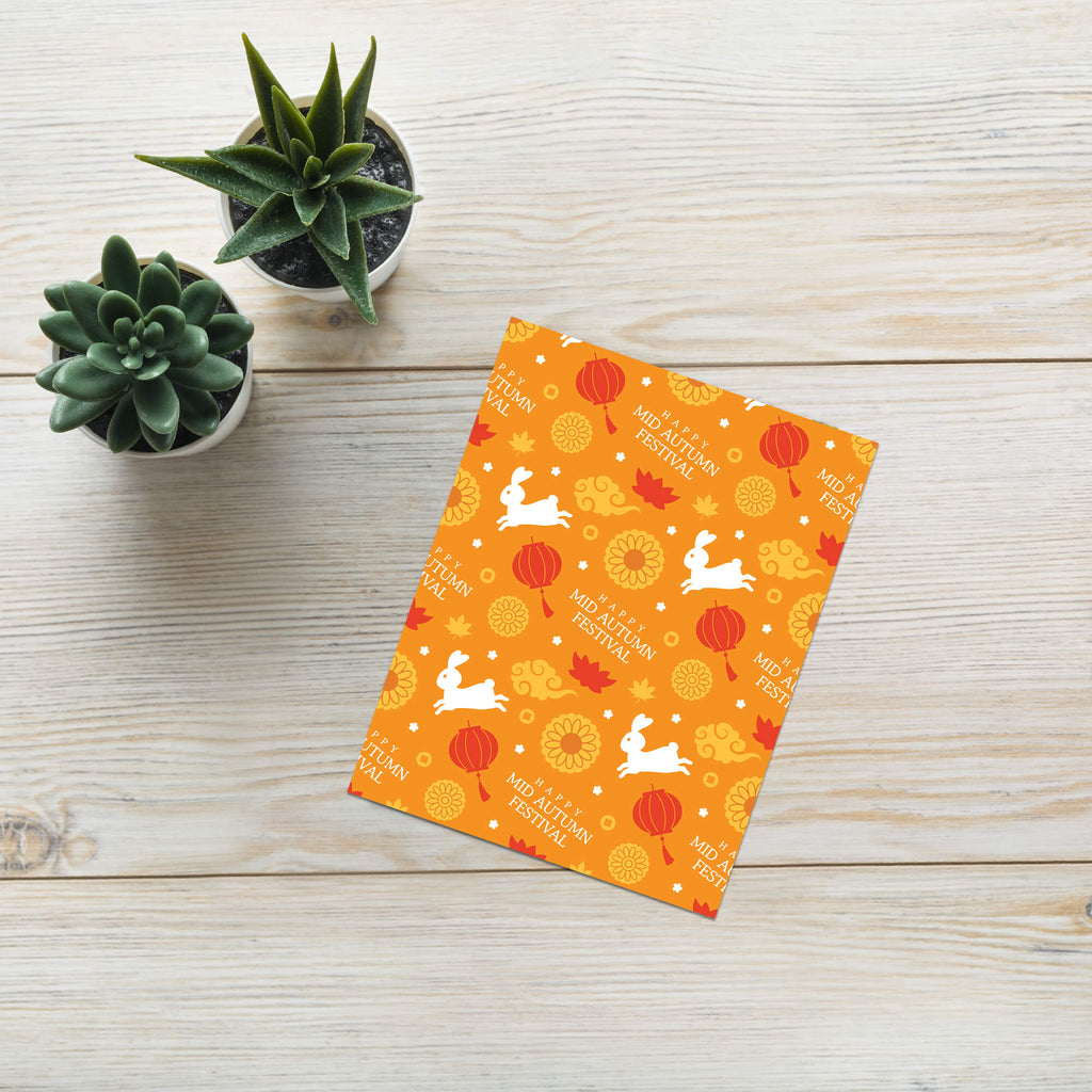 Orange greeting card for mid autumn festival  with rabbit and moon design on a wooden surface with succulents.