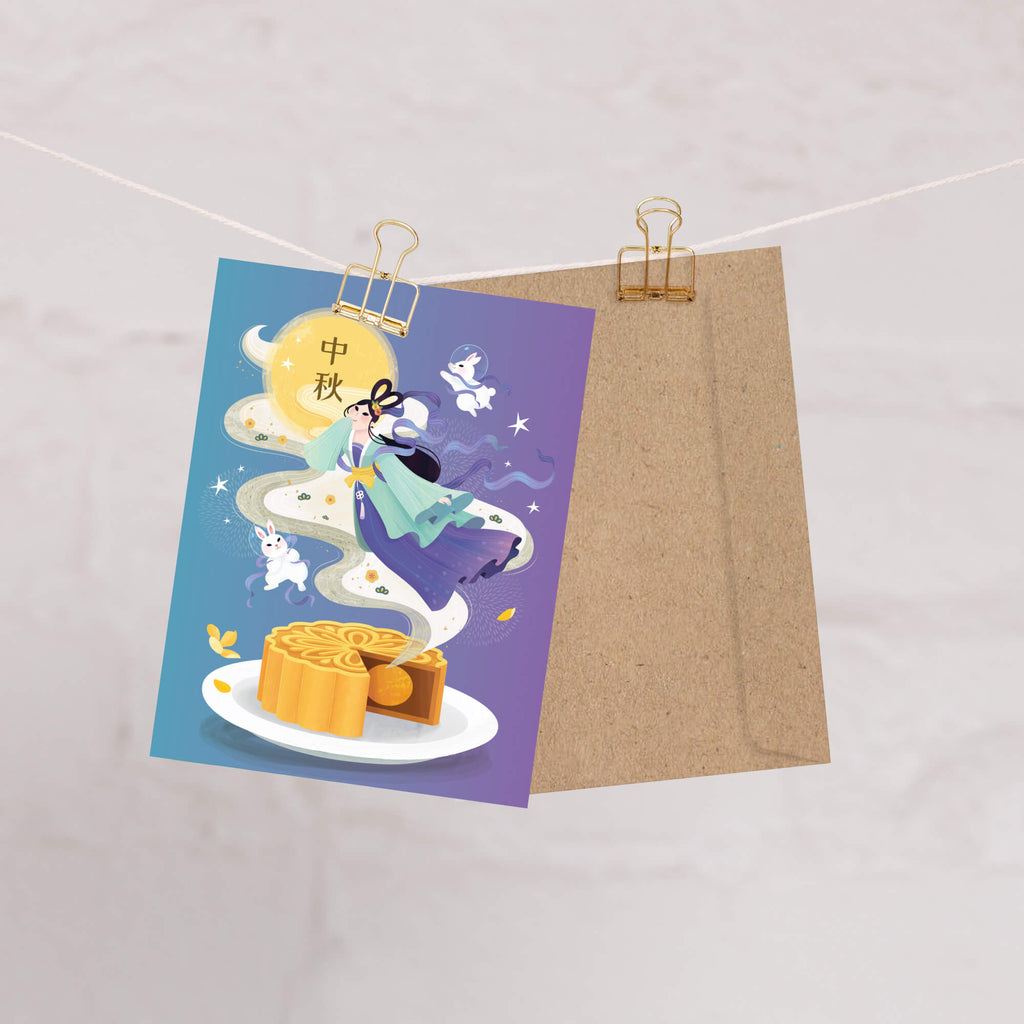 chinese Greeting card with mooncake illustration and traditional Chang E illustration with white jade rabbits and mooncake on a purple background, clipped to a string.