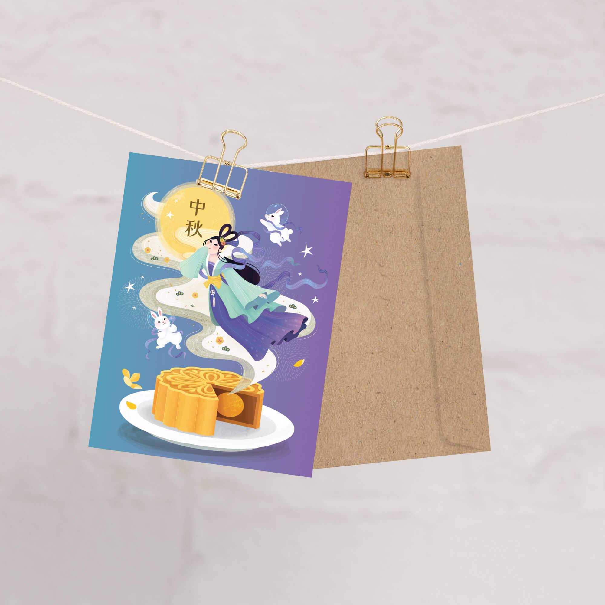 chinese Greeting card with mooncake illustration and traditional Chang E illustration with white jade rabbits and mooncake on a purple background, clipped to a string.