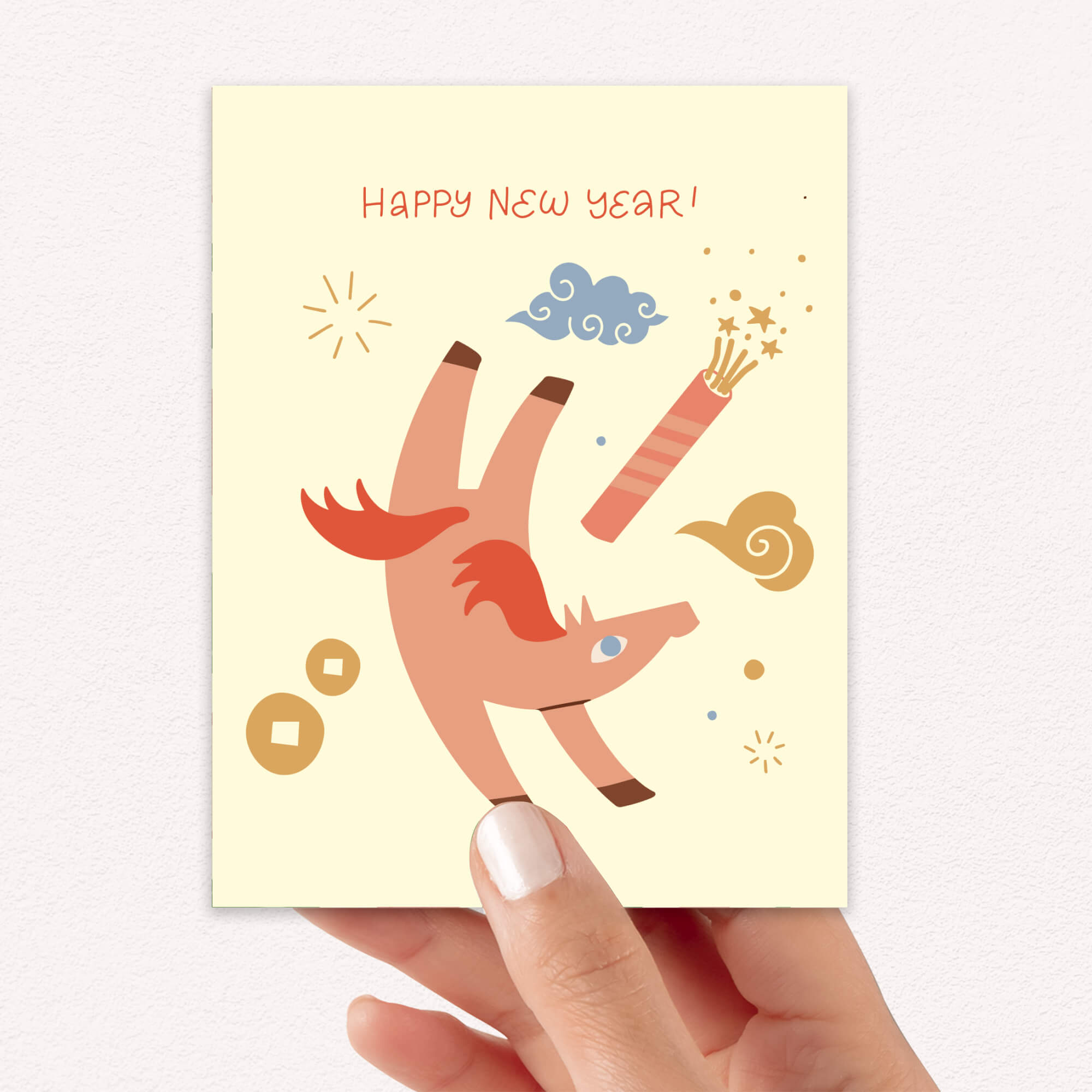 Hand holding a chinese New Year's card with a year of the horse and fireworks illustration on a light yellow background.