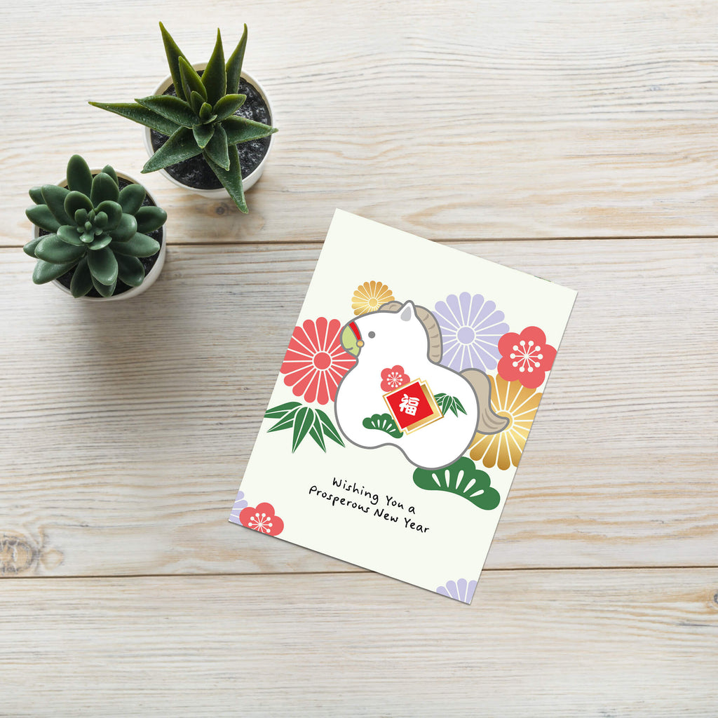 japanese lunar new year Greeting card with a horse illustration and floral elements on a wooden surface with small potted plants.
