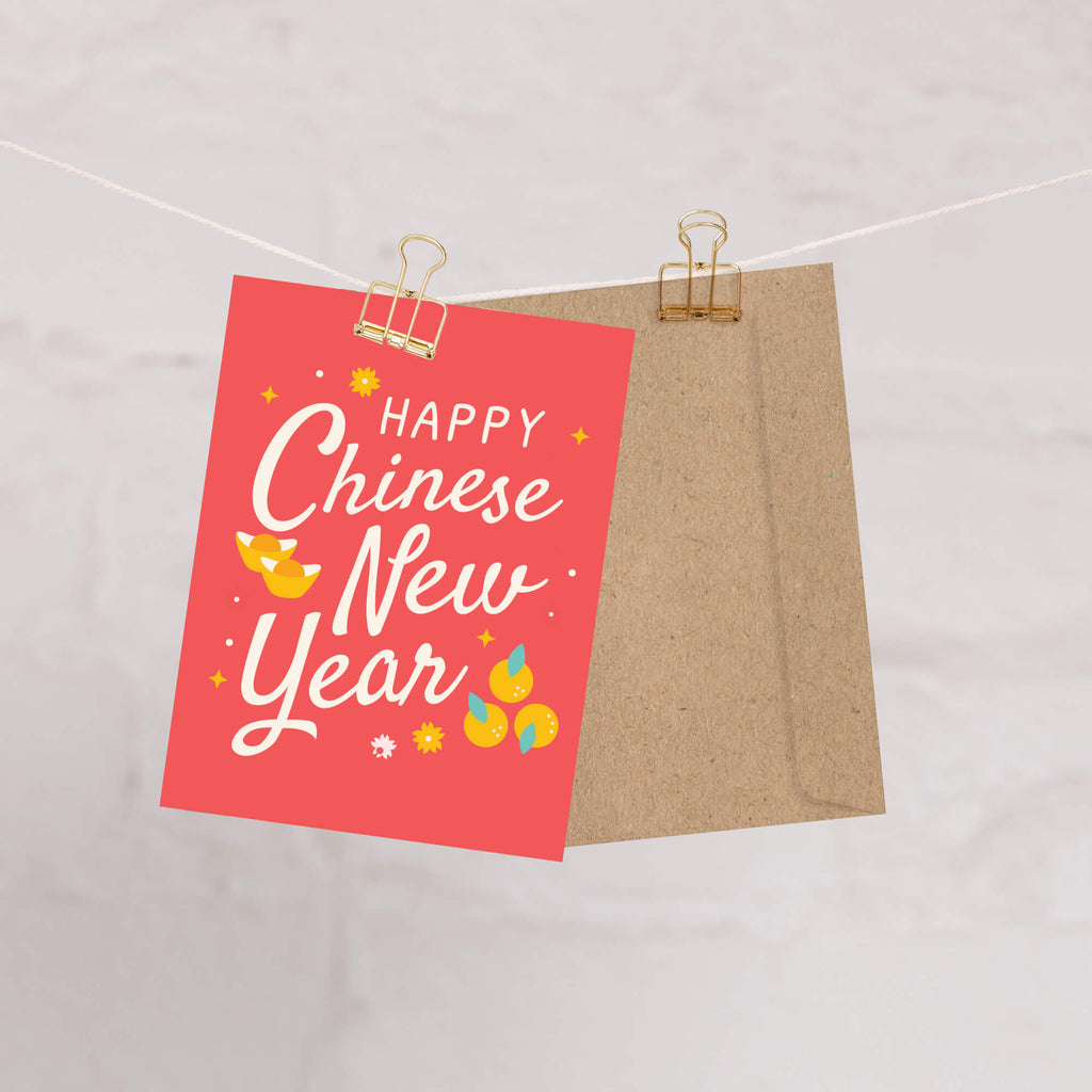 Card with 'Happy Chinese New Year' text and illustrations on a pink background, clipped to a string.