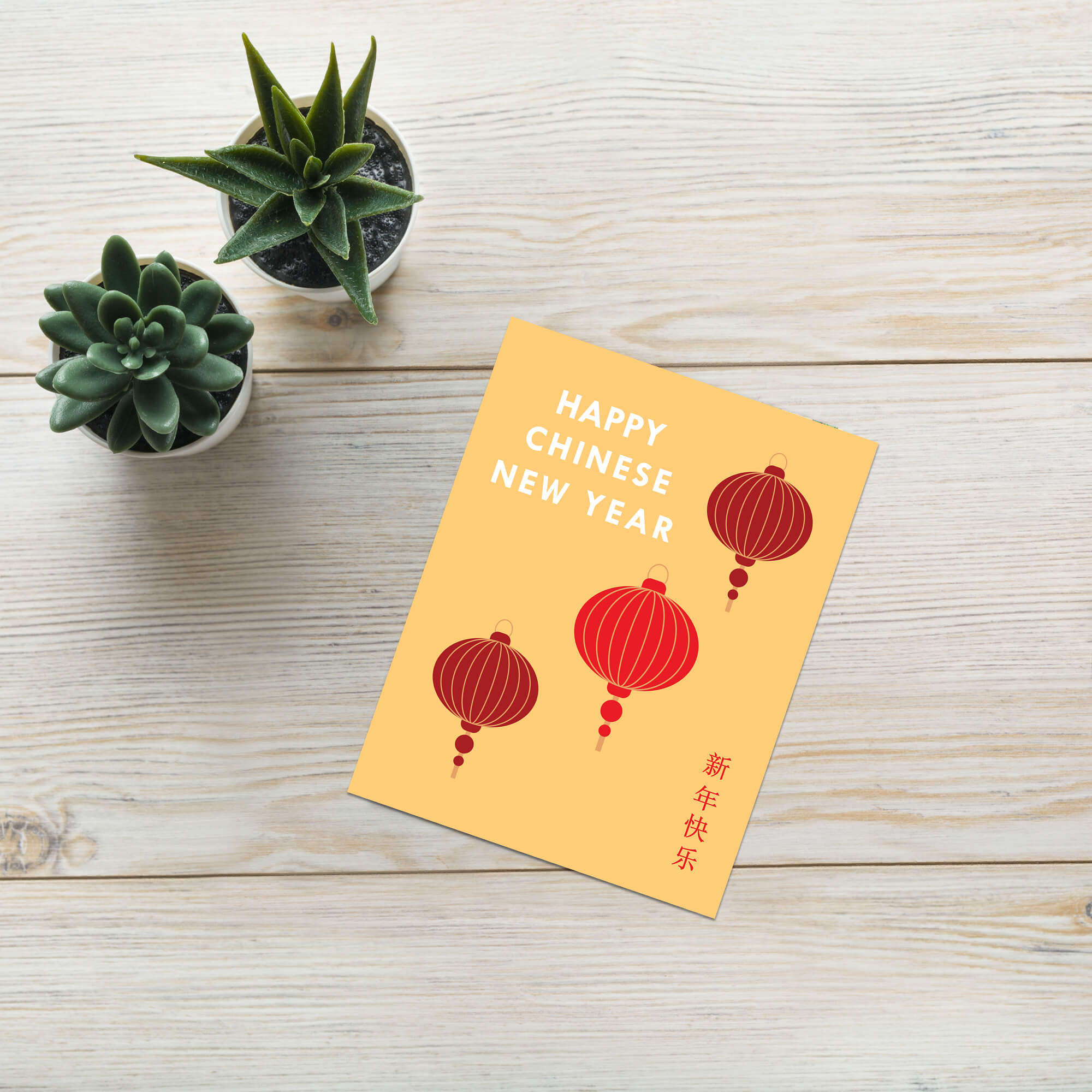 Happy Chinese New Year card with red lanterns on a wooden surface with small potted plants.