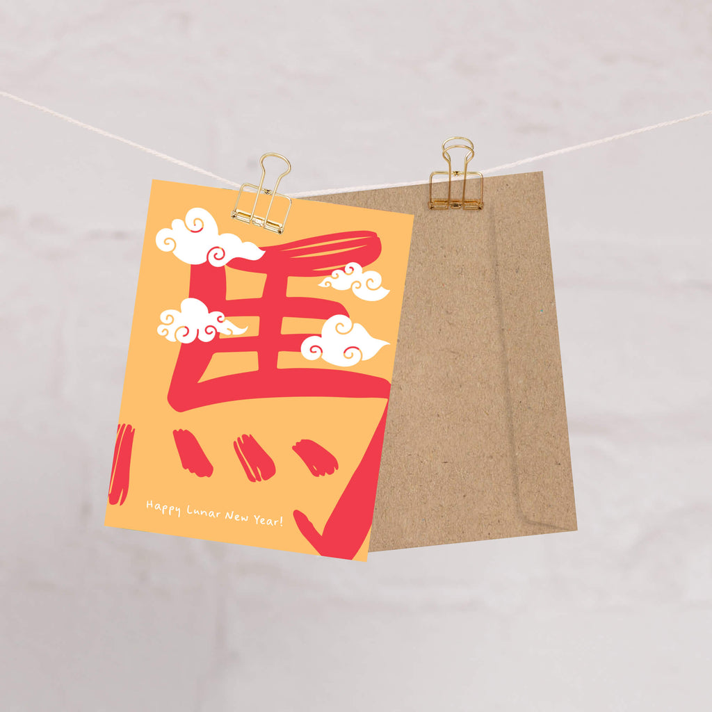 Card with red and yellow design and 'Happy Lunar New Year!' text, hanging on a string.