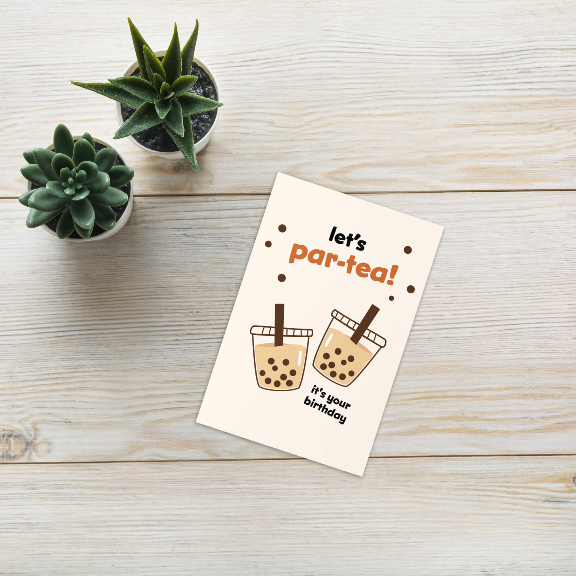 Greeting card with 'let's par-tea! It's your birthday' text on a wooden surface with small plants.