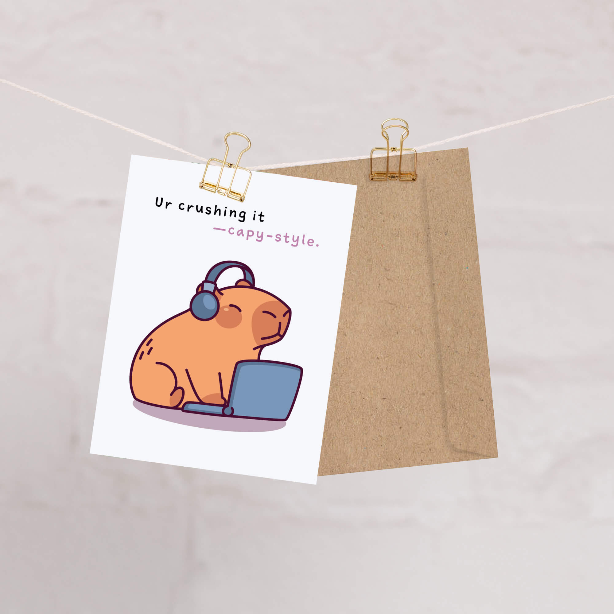 Card with a cartoon cat wearing headphones and using a laptop, pinned to a string with a brown envelope.