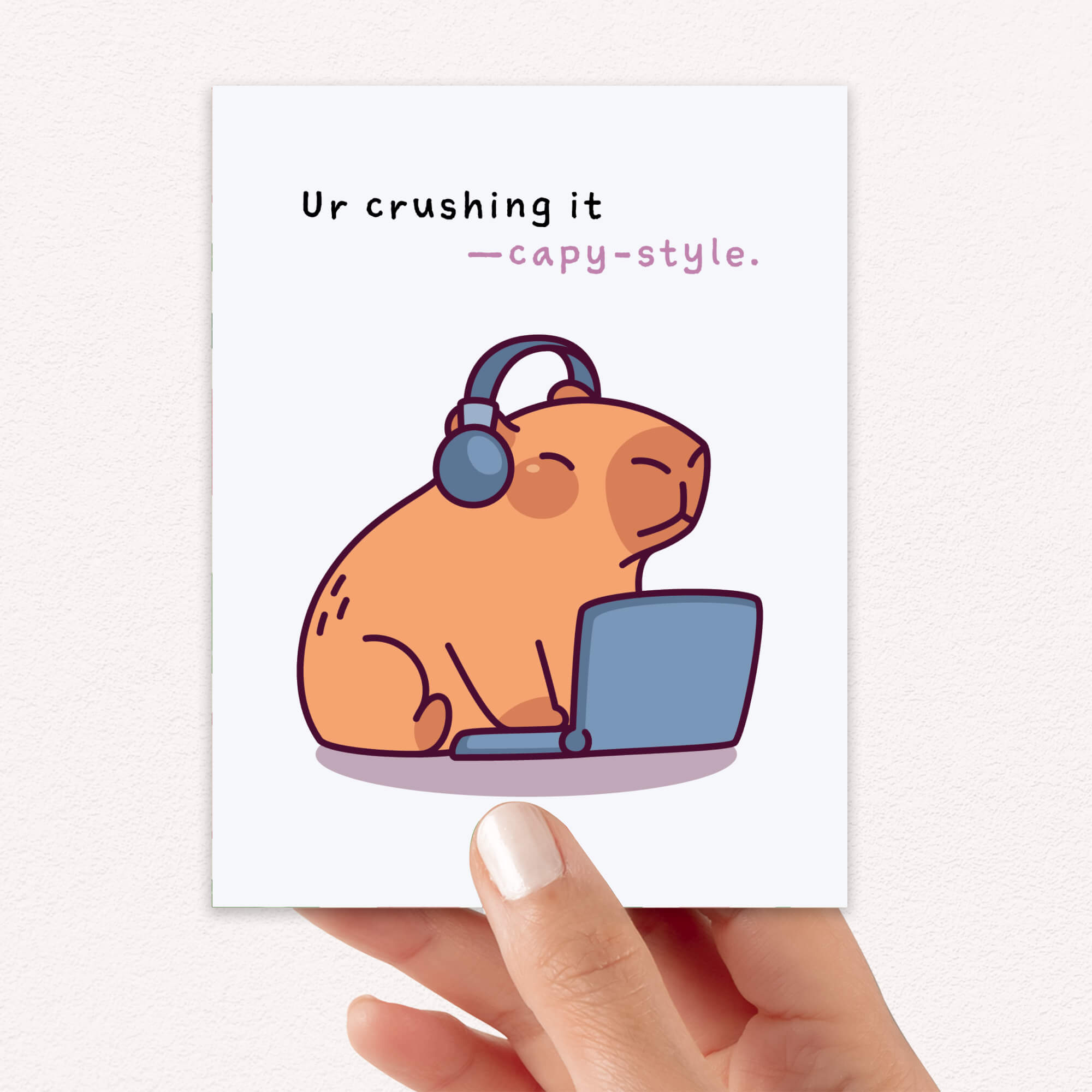 Illustration of a guinea pig wearing headphones and using a laptop with text 'Ur crushing it capy-style' held by a hand.