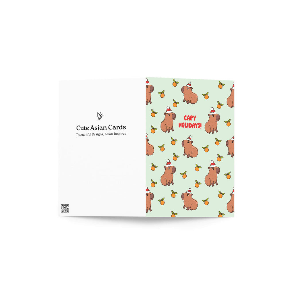 cute christmas card with Repeating pattern of capybaras in Santa hats with small oranges on a pale green background. Text reads a pun: “Capy Holidays.”