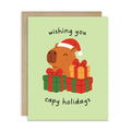 cute unique Christmas card with a capybara wearing a Santa hat and surrounded by presents on a light green background with text pun: wishing you capy holidays