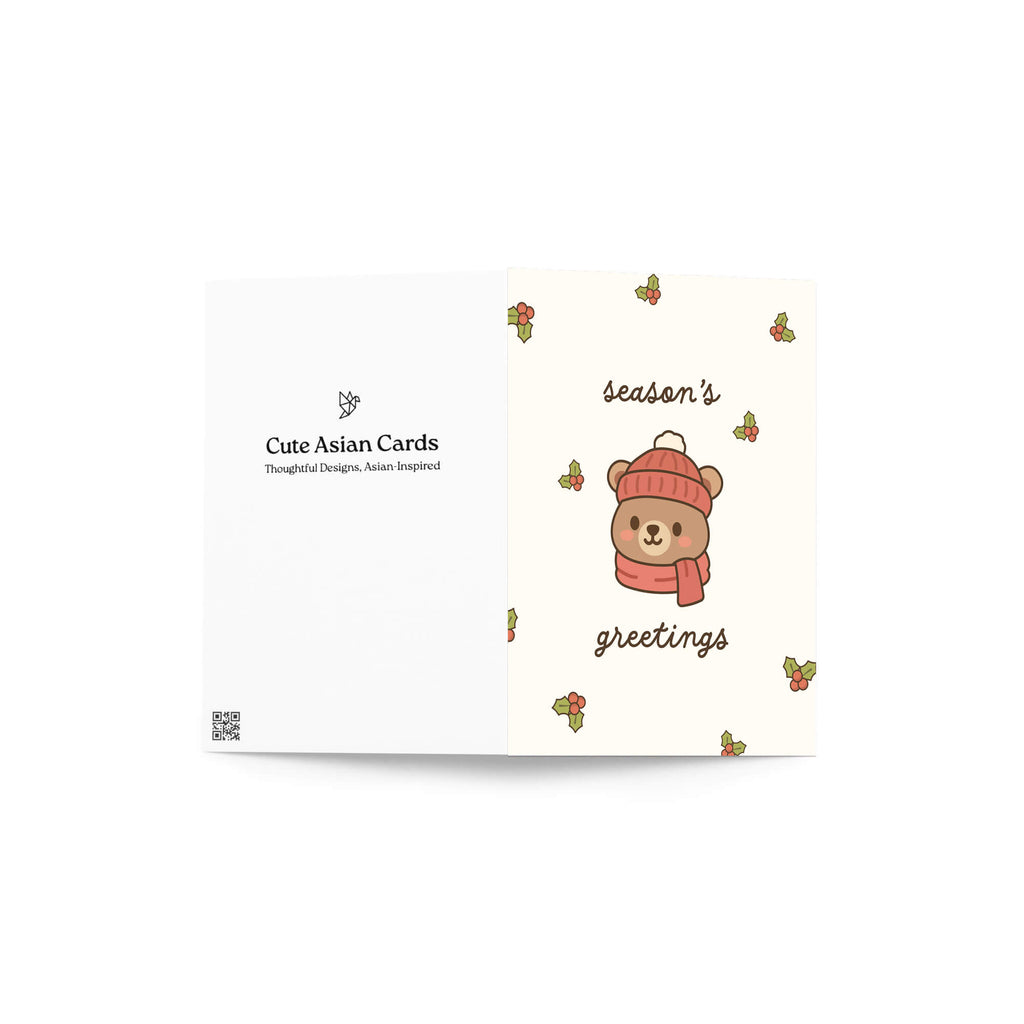 cute Christmas card with a bear wearing a pink hat and scarf, surrounded by holly leaves and berries with text: season's greetings
