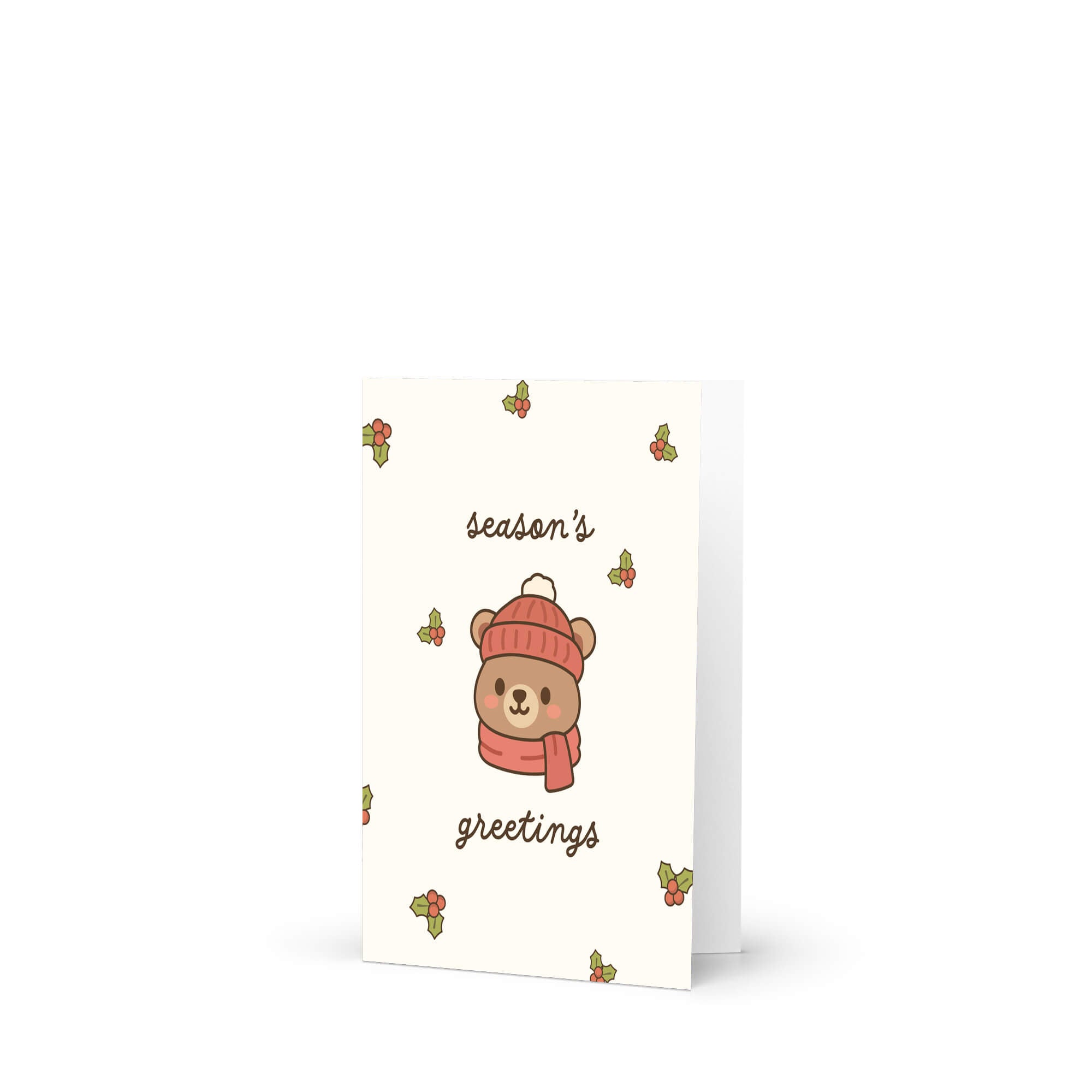 cute Christmas card with a bear wearing a pink hat and scarf, surrounded by holly leaves and berries with text: season's greetings