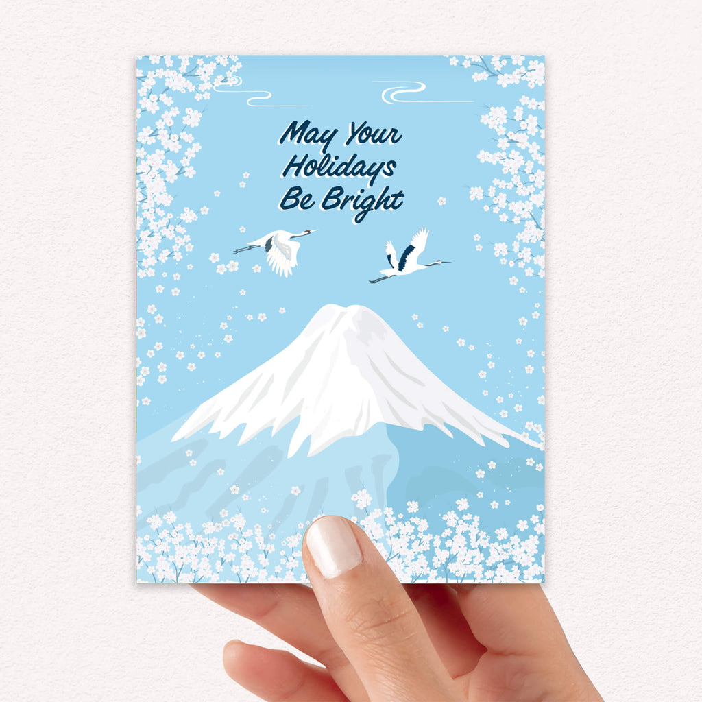 japanese christmas card with a winter snowy Mount Fuji with cranes and white cherry blossoms; text “May Your Holidays Be Bright.”