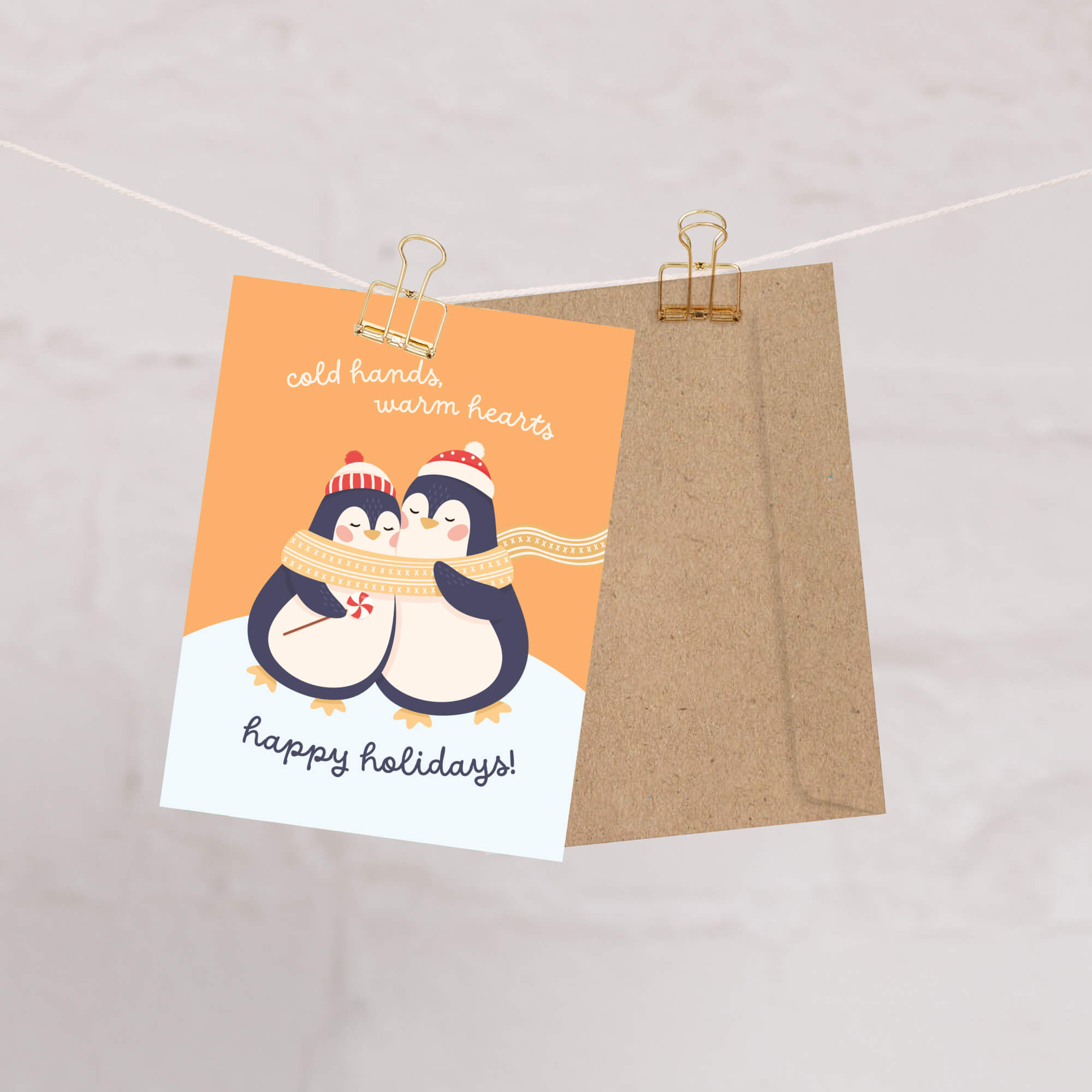 unique holiday card with two penguins hugging, wearing scarves and hats, on an orange background with text "Two penguins in knit hats sharing a scarf; text “cold hands, warm hearts — happy holidays!”"