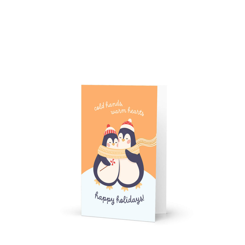unique holiday card with two penguins hugging, wearing scarves and hats, on an orange background with text "Two penguins in knit hats sharing a scarf; text “cold hands, warm hearts — happy holidays!”"