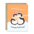 unique holiday card with two penguins hugging, wearing scarves and hats, on an orange background with text "Two penguins in knit hats sharing a scarf; text “cold hands, warm hearts — happy holidays!”"