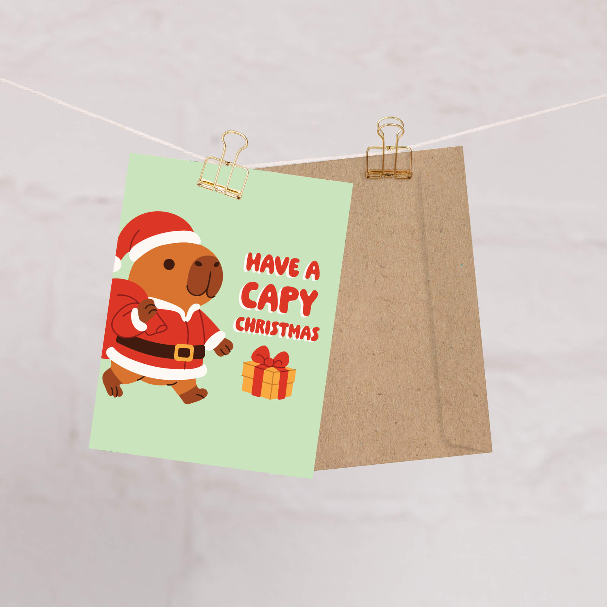 cute unique Christmas card with a capybara in a Santa outfit and text 'Have a Capy Christmas' on a light green background.