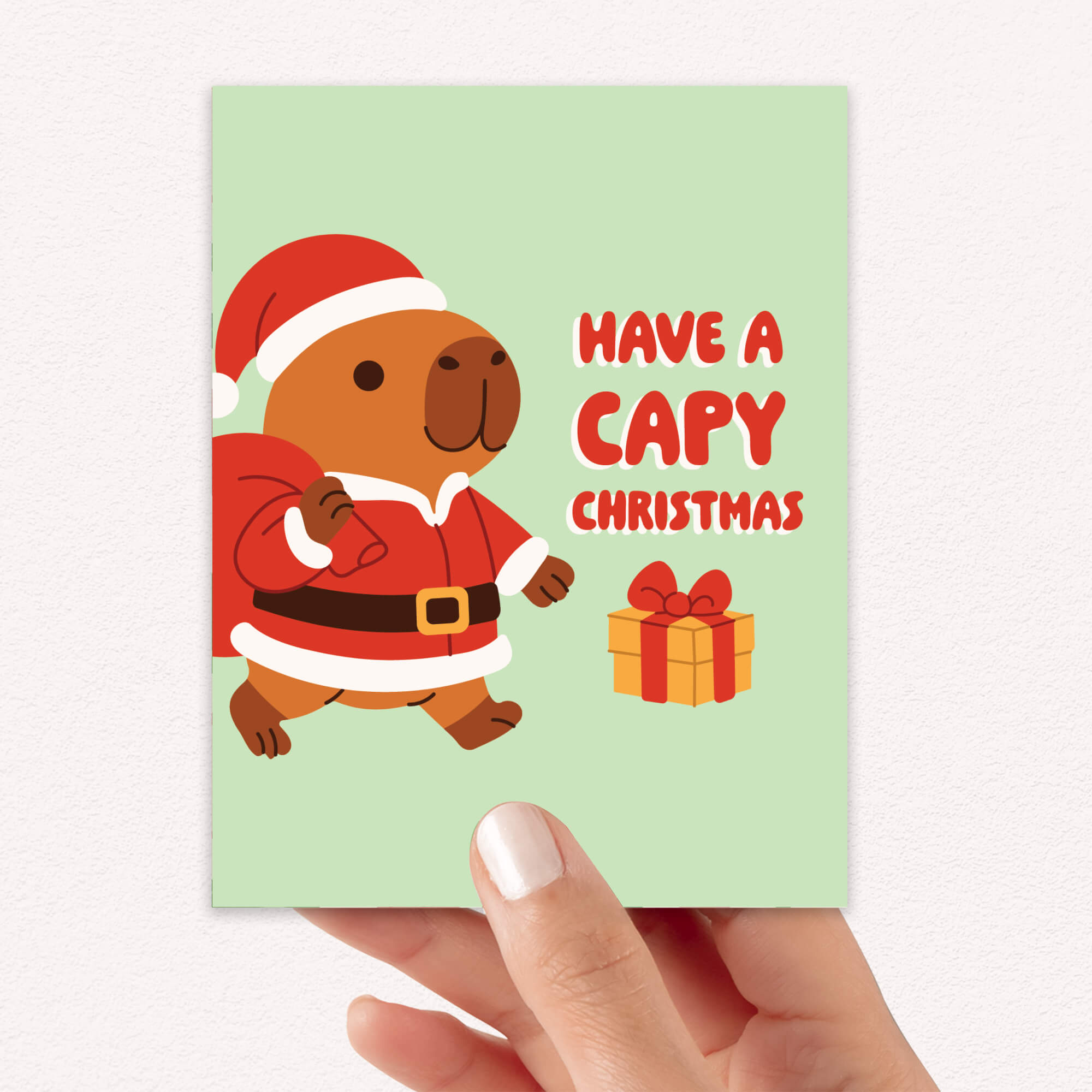 cute unique Christmas card with a capybara in a Santa outfit and text 'Have a Capy Christmas' on a light green background.