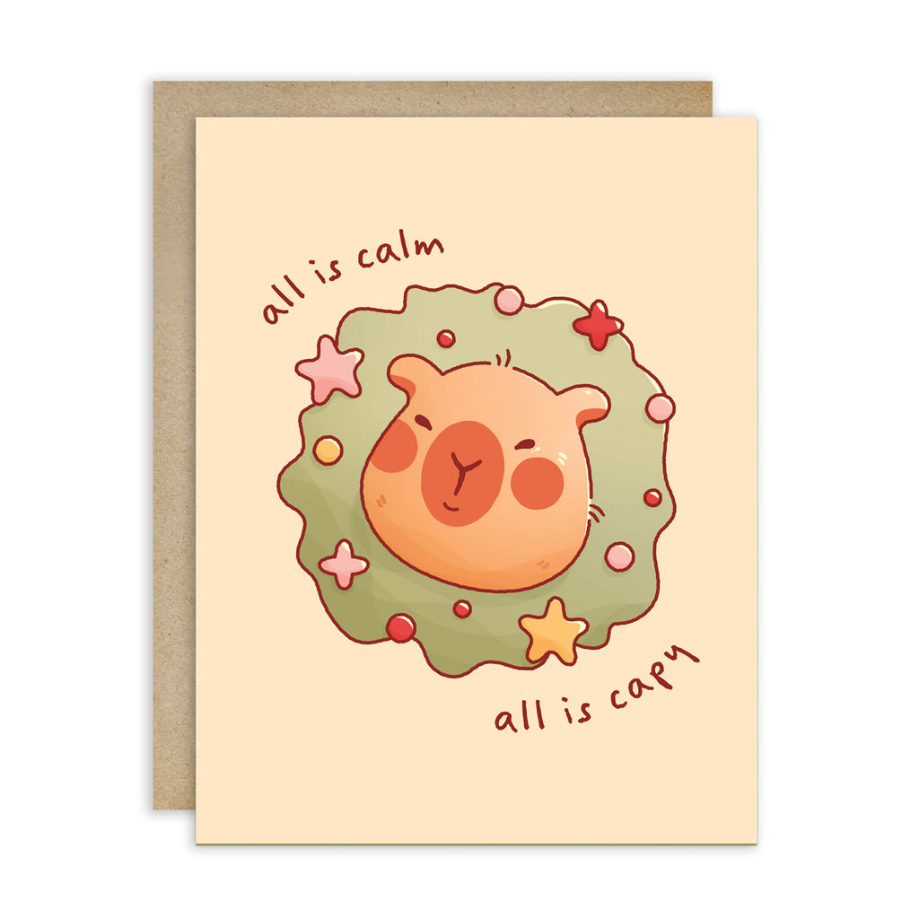 cute christmas card with a Capybara nestled in green holiday wreath with stars, text “all is calm, all is capy.”