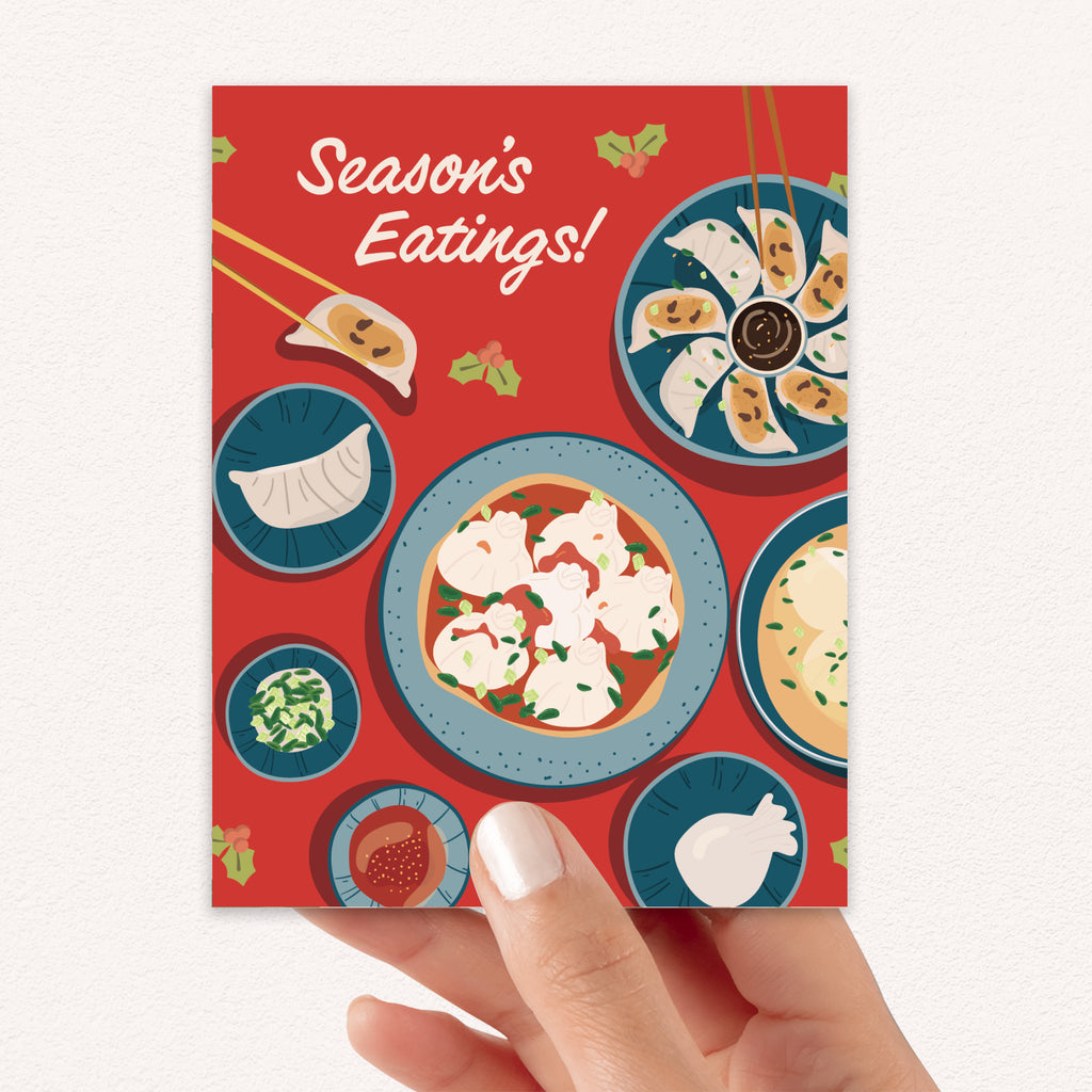 cute christmas card showing a red table with plates of dumplings and sauces, text “Season’s Eatings!”