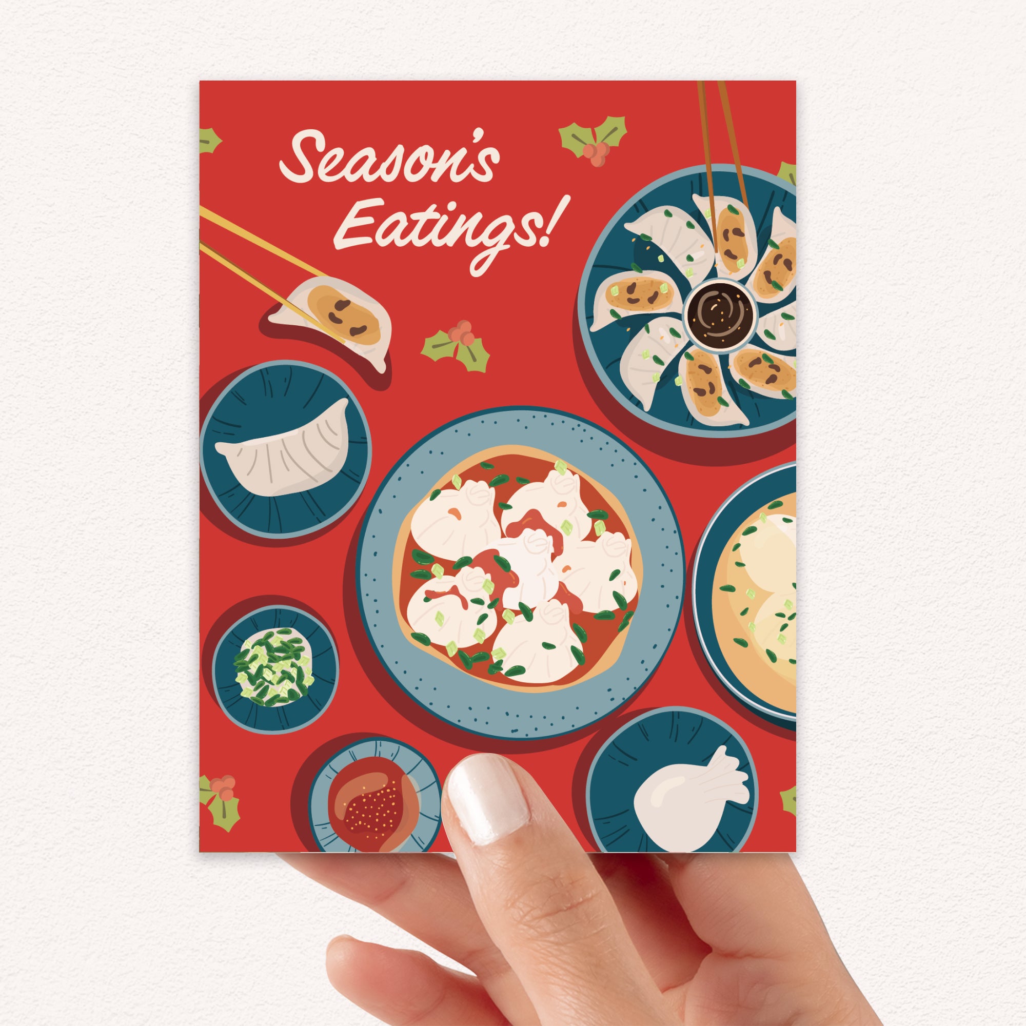 cute christmas card showing a red table with plates of dumplings and sauces, text “Season’s Eatings!”