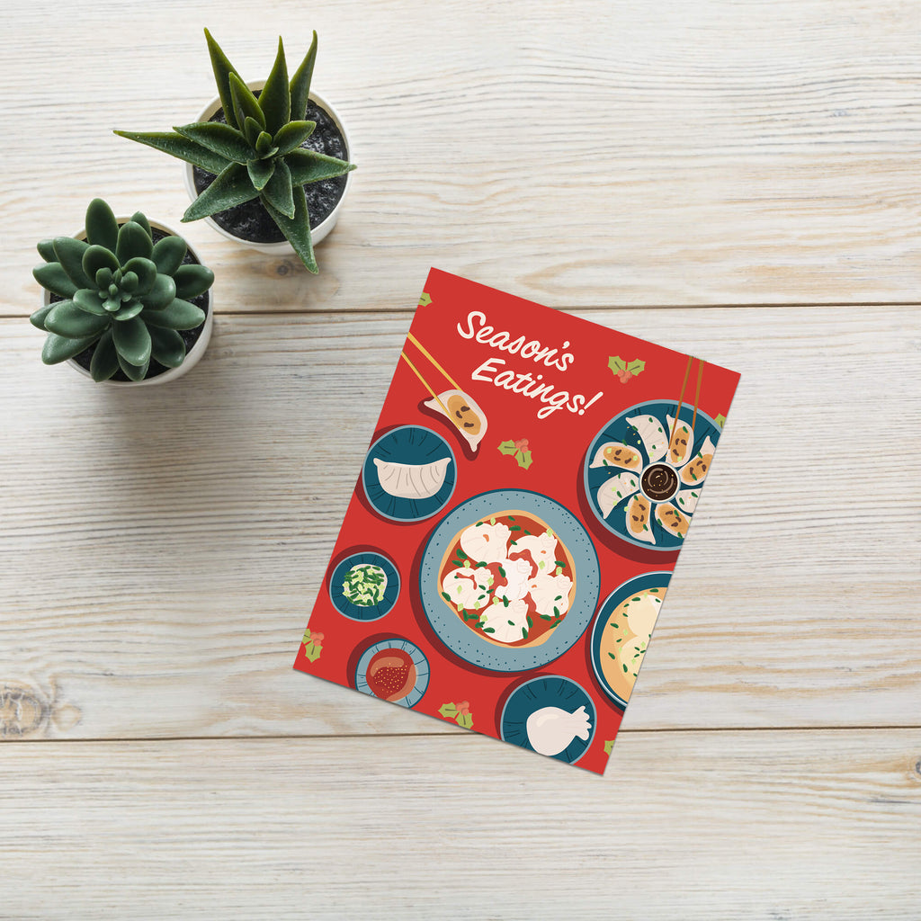 cute christmas card showing a red table with plates of dumplings and sauces, text “Season’s Eatings!”