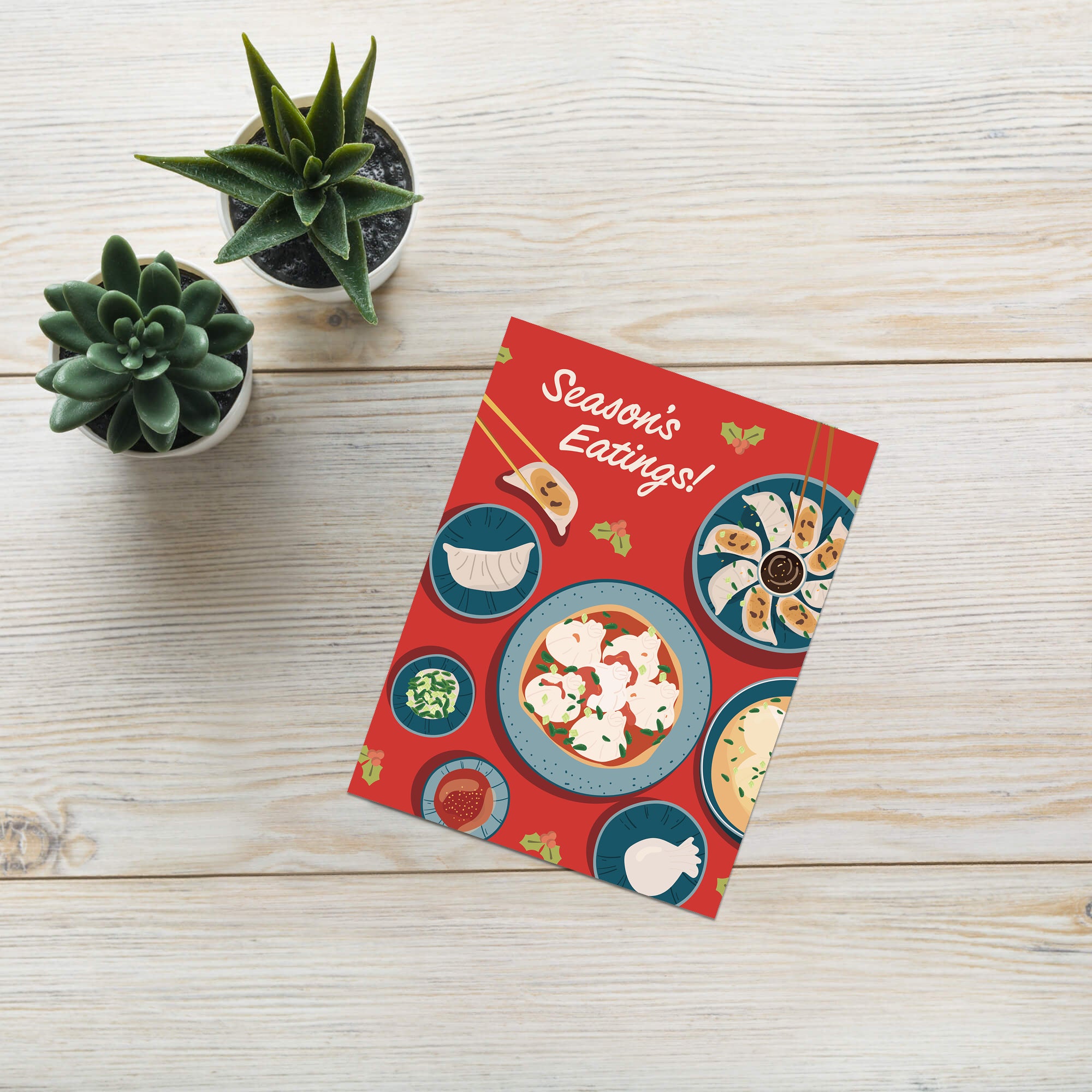 cute christmas card showing a red table with plates of dumplings and sauces, text “Season’s Eatings!”