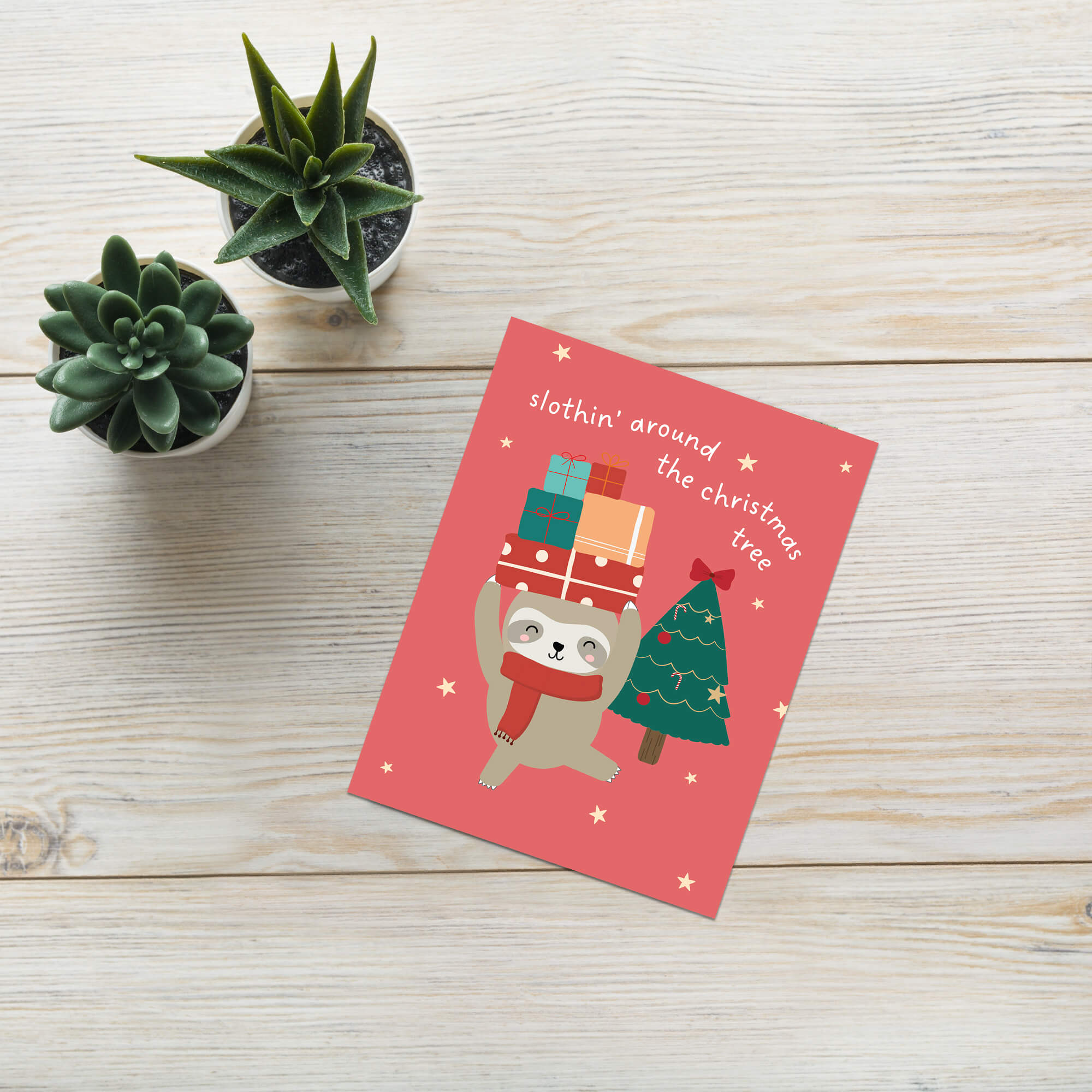 unique Christmas card with a sloth carrying presents and a holiday tree on a red background with text "slothin' around the christmas tree"