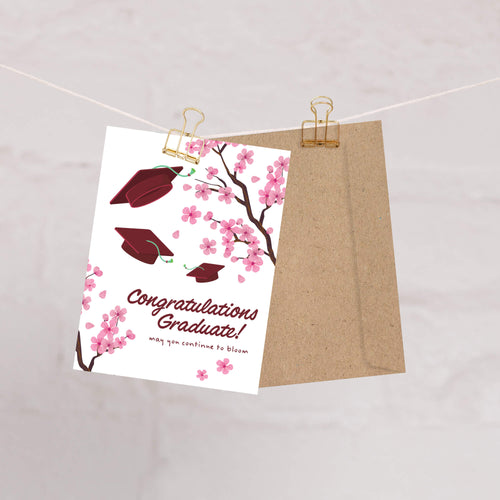 Graduation card with japanese cherry blossoms and red graduation caps on a white background