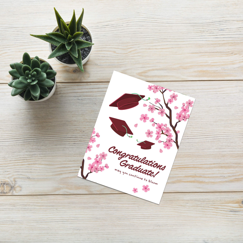Graduation card with japanese cherry blossoms and red graduation caps on a white background