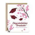 Graduation card with japanese cherry blossoms and red graduation caps on a white background