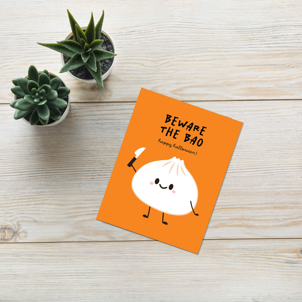 Orange card with a cartoon bao bun and text 'Beware the Bao' on a wooden surface with small plants.