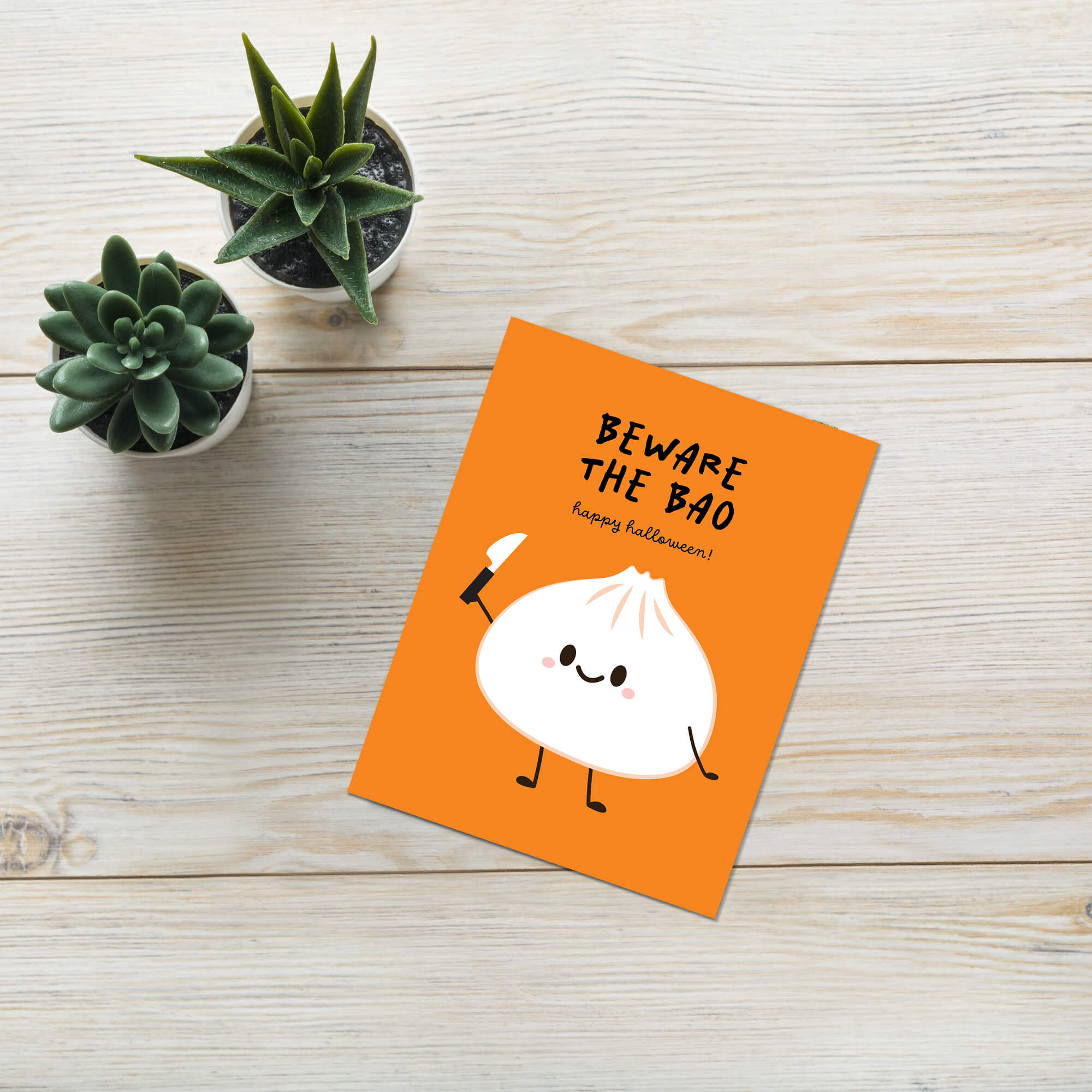 Orange card with a cartoon bao bun and text 'Beware the Bao' on a wooden surface with small plants.