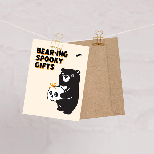 Halloween-themed card with a bear holding a skull and text 'Bear-ing Spooky Gifts' on a beige background.
