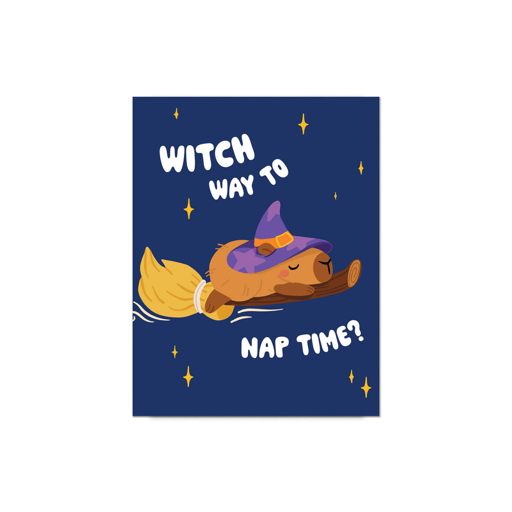 Halloween-themed greeting card with a capybara in a witch hat and broom, text 'Witch way to nap time?' on a blue background, clipped to a string.