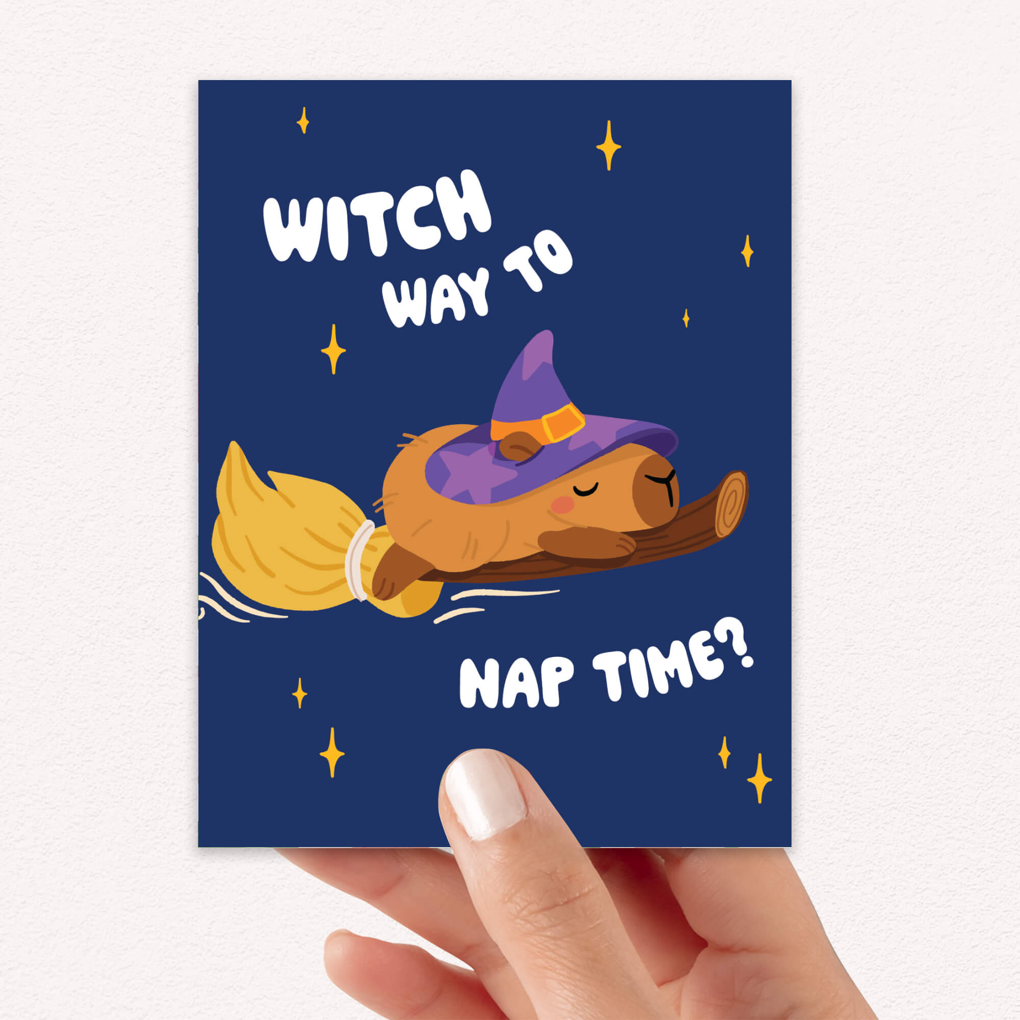 Halloween-themed greeting card with a capybara in a witch hat and broom, text 'Witch way to nap time?' on a blue background