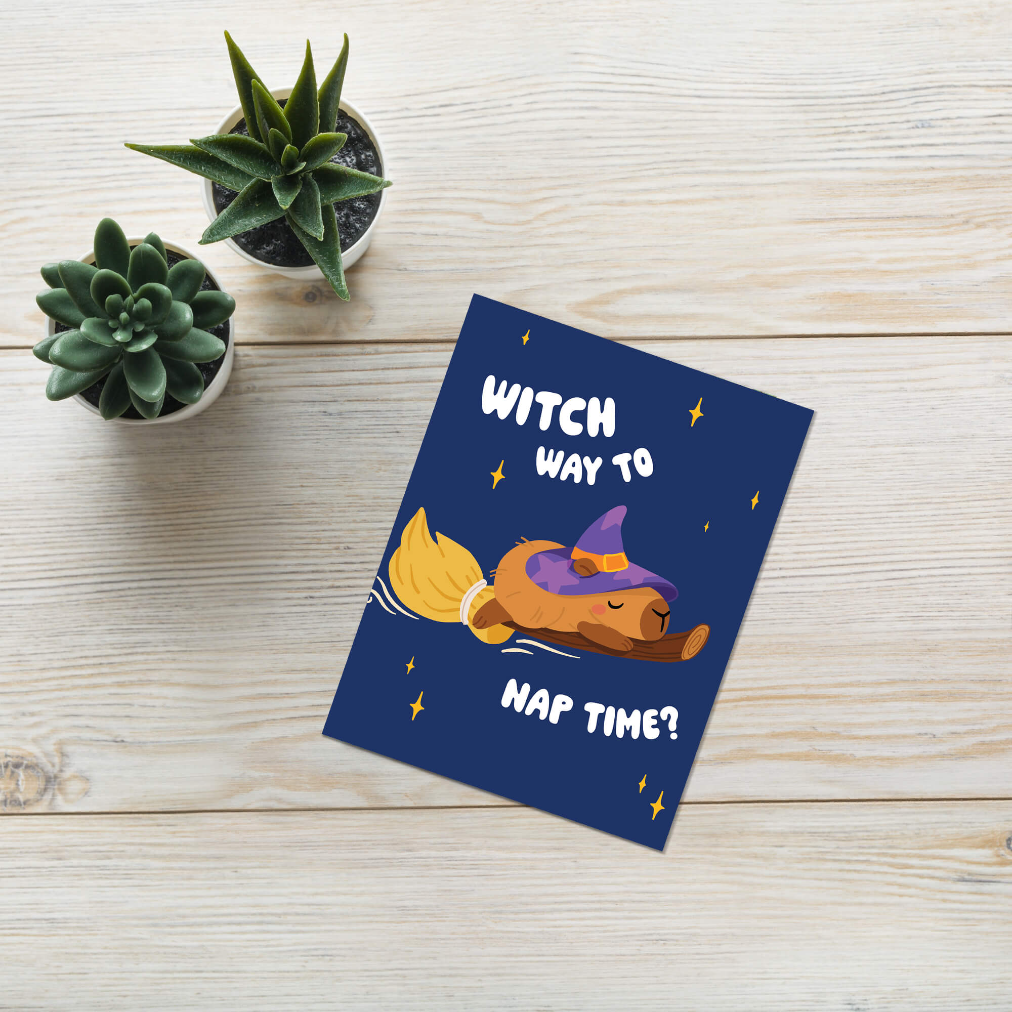 cute Halloween-themed greeting card with a capybara in a witch hat and broom, text 'Witch way to nap time?' on a blue background