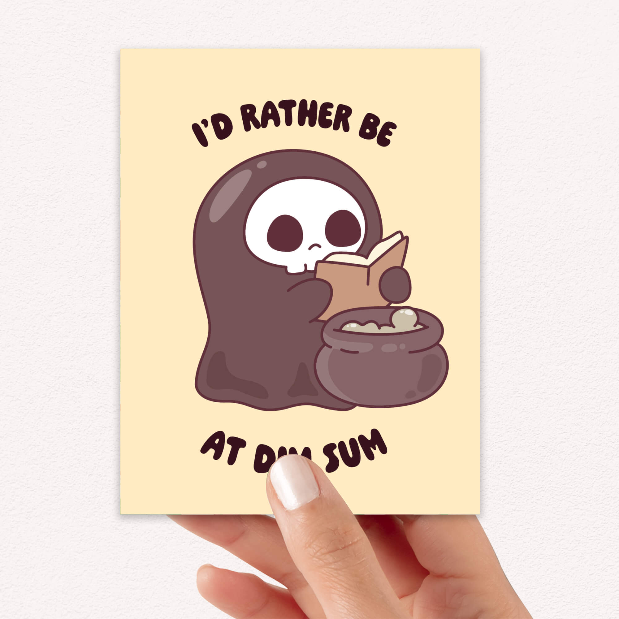 funny halloween Greeting card with a kawaii grim reaper holding a cauldron and text 'I'd rather be at dim sum' on a beige background.
